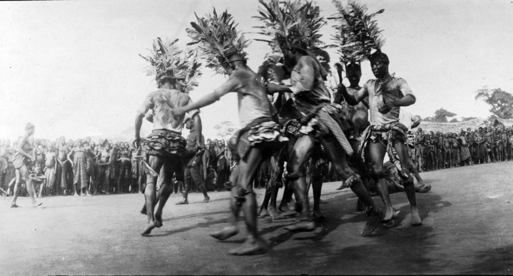 Archival black-and-white photo of Igbo youths dancing in a village clearing.”