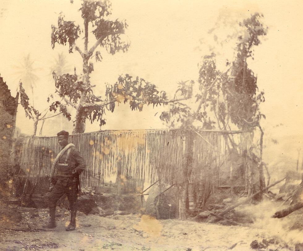 A sentry stands amid the ruins of Arochukwu during the 1901 Aro Expedition. Photographed by Donald A. MacAlister.