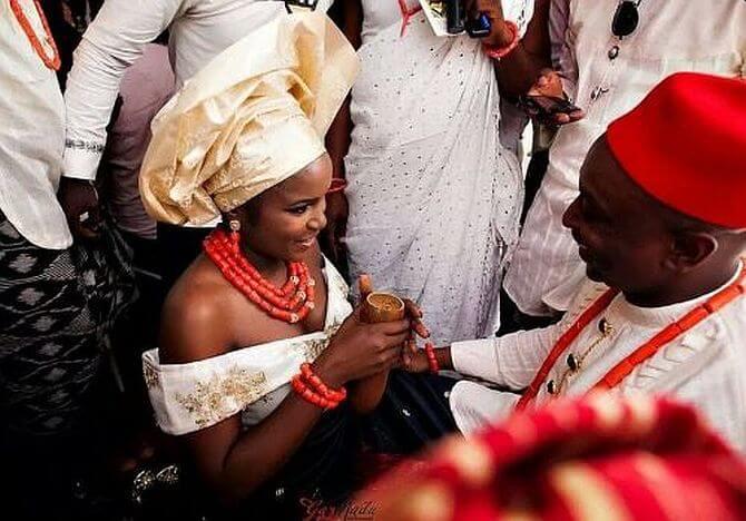 Igbo bride kneeling and offering palm wine to groom.