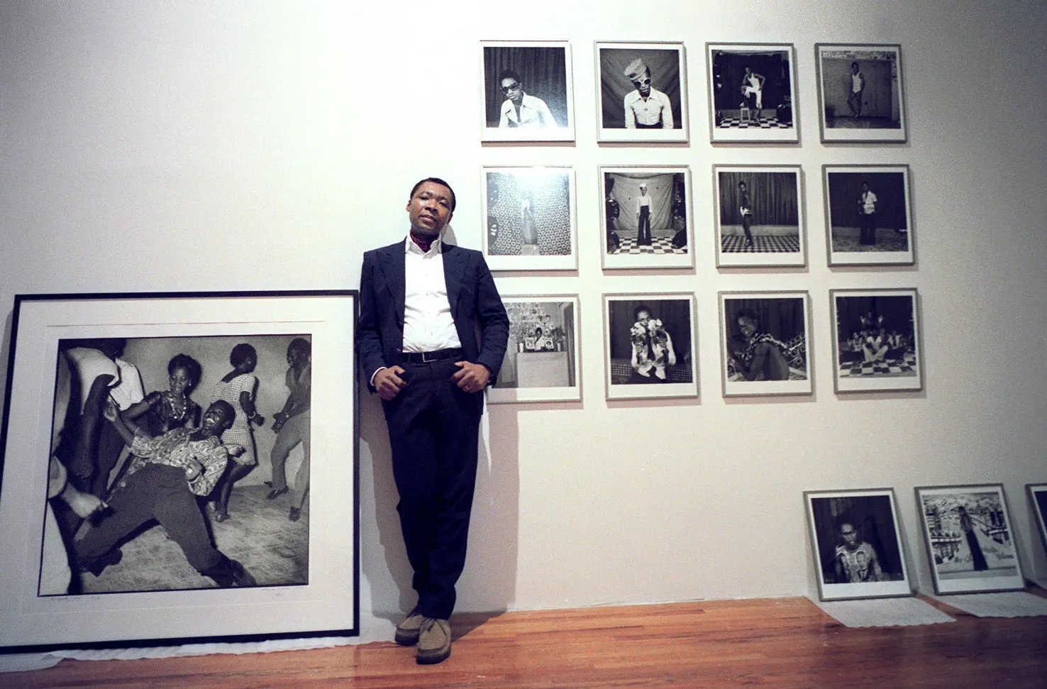 Okwui Enwezor in 2002 as he prepared the exhibition "Short Century: Independence and Liberation Movements in Africa 1945-1994,* at what is now MoMA PSI. The work of Samuel Fosso is on the wall. Edward Keating/The New York Times