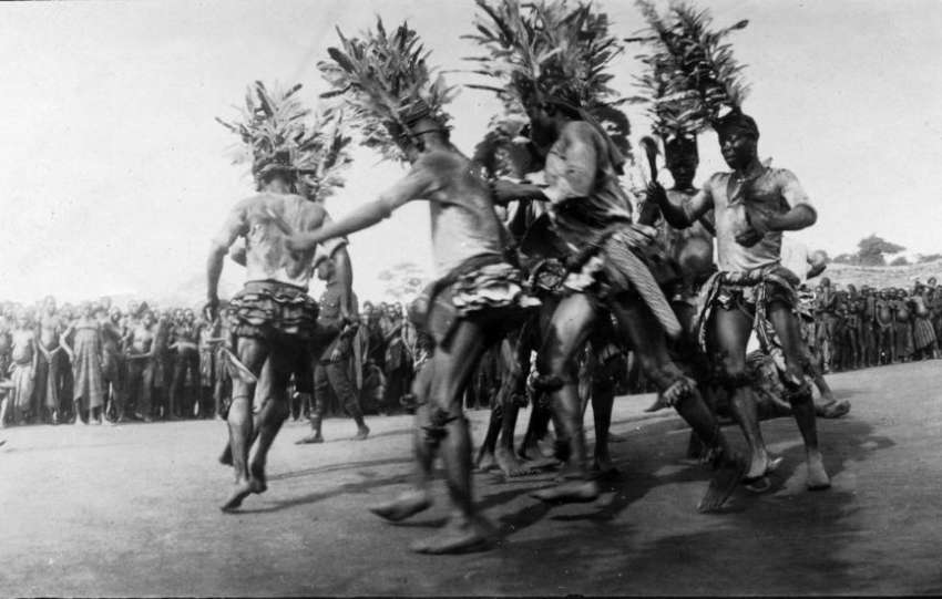 Archival black-and-white photo of Igbo youths dancing in a village clearing.”
